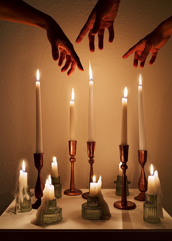 three hands hover above a table filled with lit candles