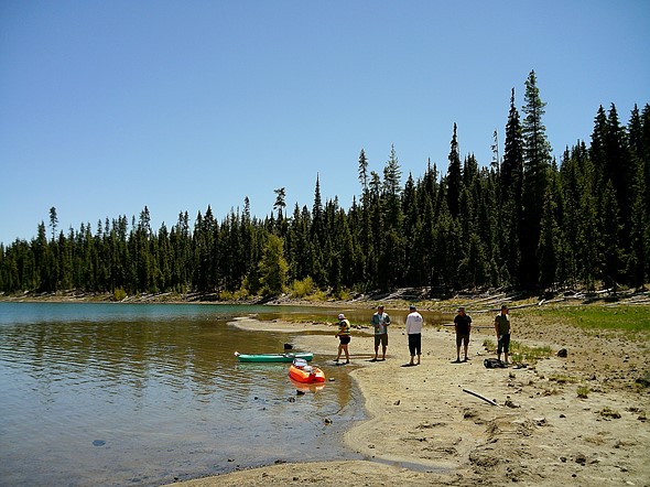 Quatre personnes sur une rive sablonneuse d'un lac avec un kayak vert et orange en eau peu profonde