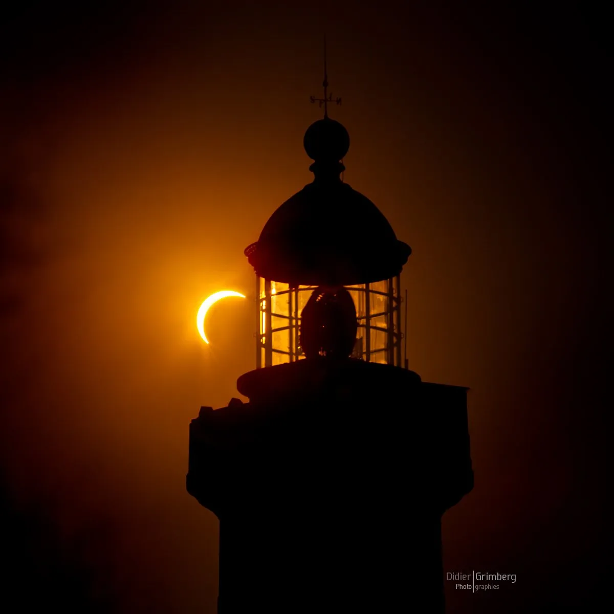 A lighthouse fills the frame, the sun an orange crescent behind it, thanks to the eclipse.