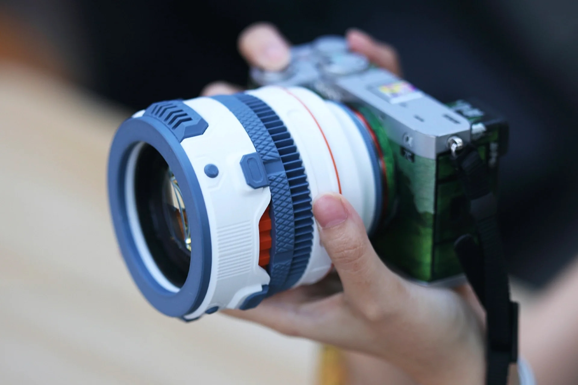 Camera with a large, uniquely designed blue and white lens held in a hand, positioned for photography.