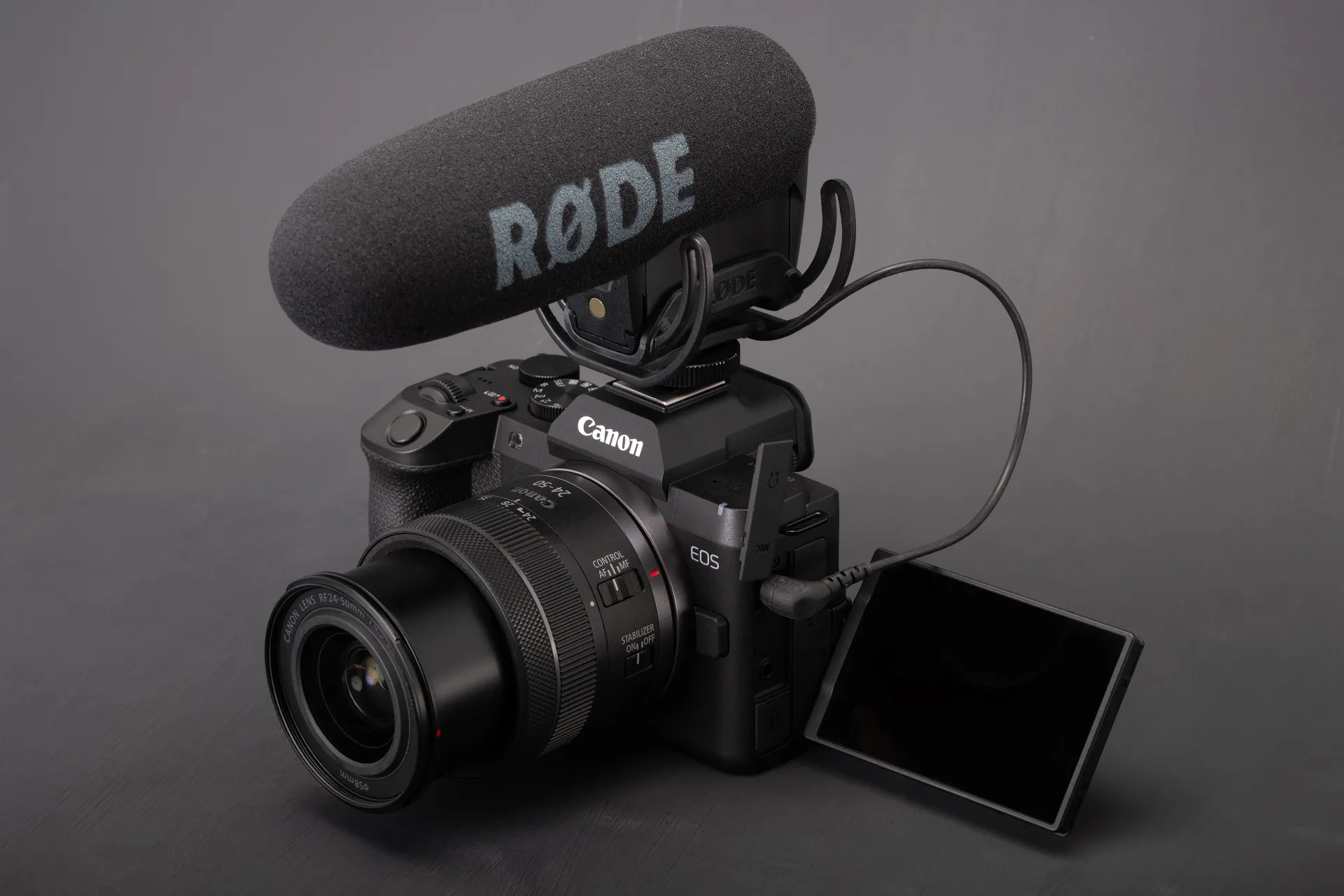 The EOS R8 II with its screen flipped out and a large shotgun microphone attached to the hotshoe.