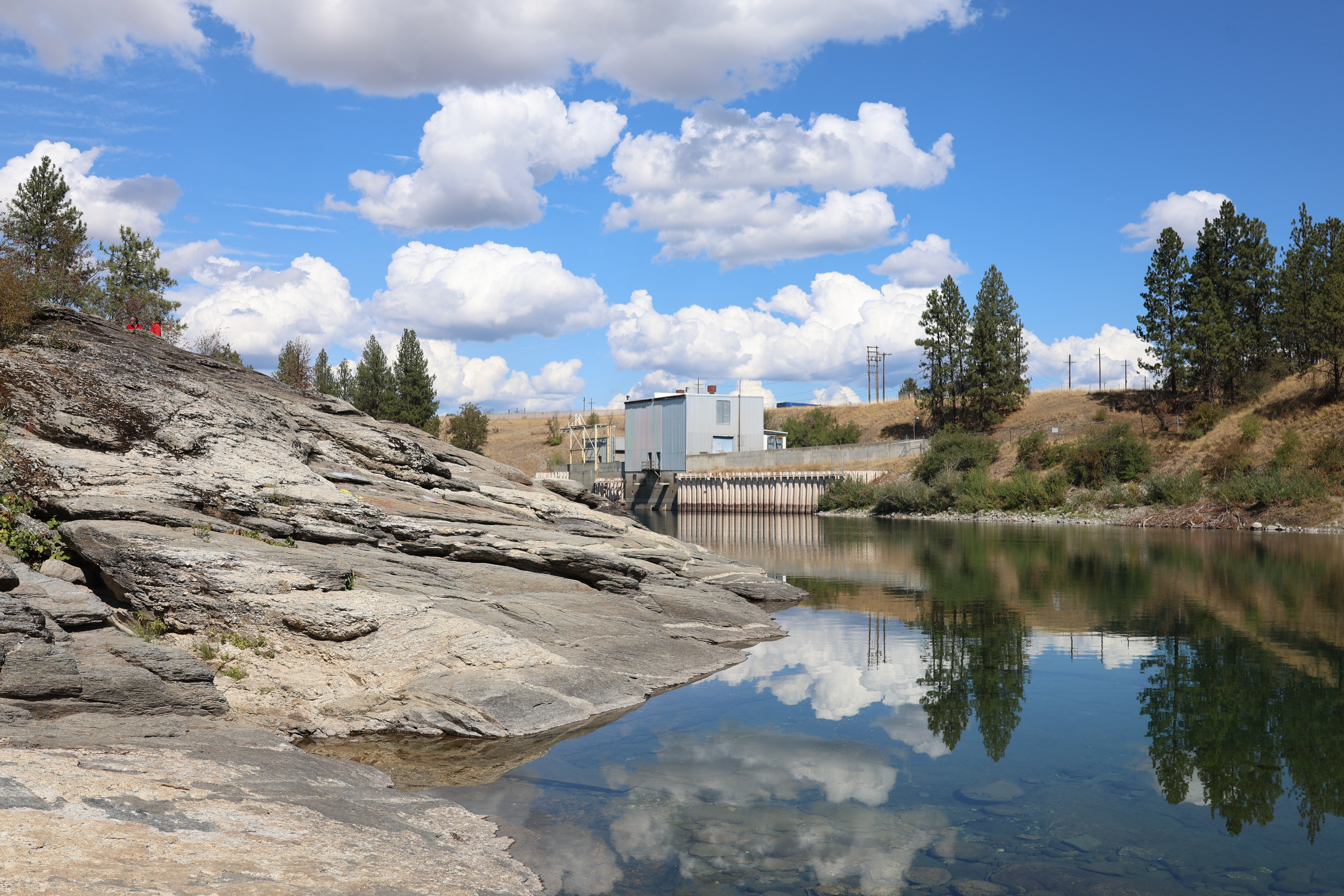 A scene with a rock slab on the left and a blue sky reflected in the Spokane River.