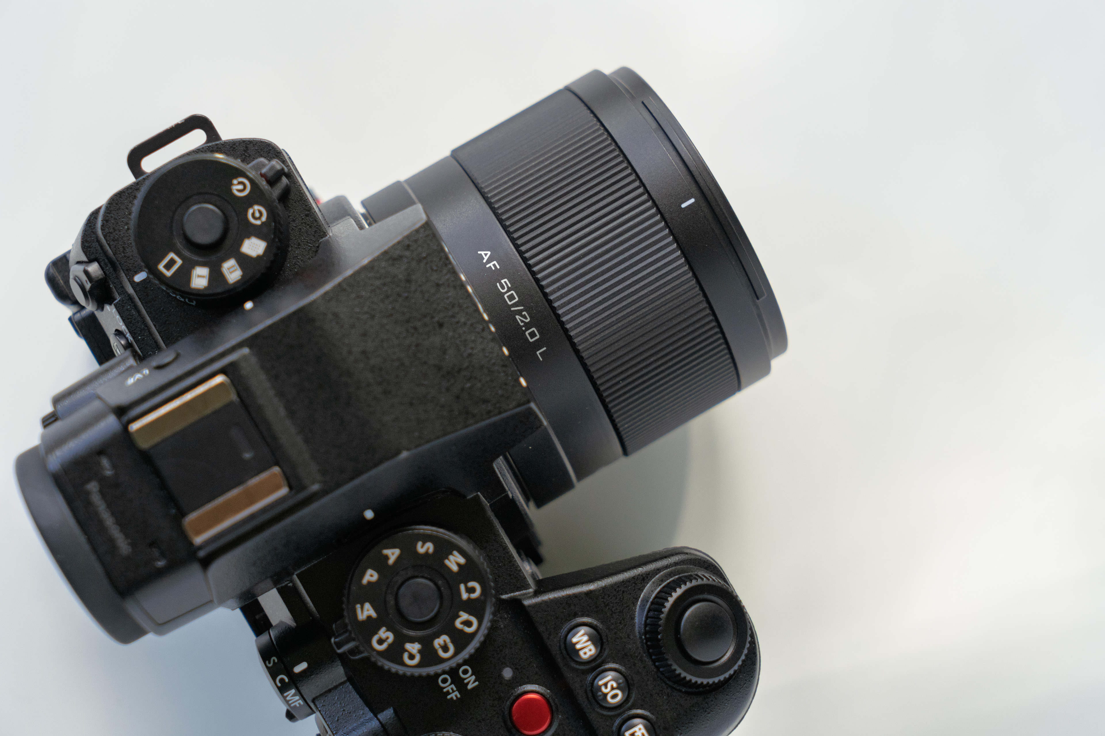 Black digital camera with a prominent lens labeled AF 50/1.2 D L, featuring clearly visible dials and buttons, resting on a white surface.