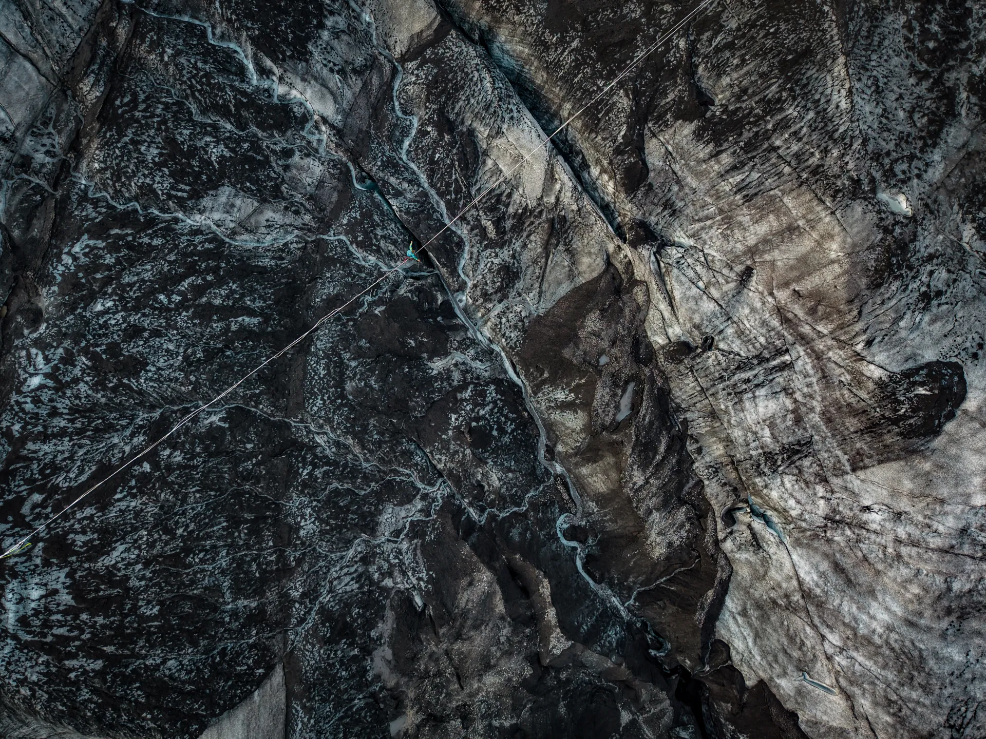 Aerial view of a dark rocky glacier with a thin rope line crossing diagonally.