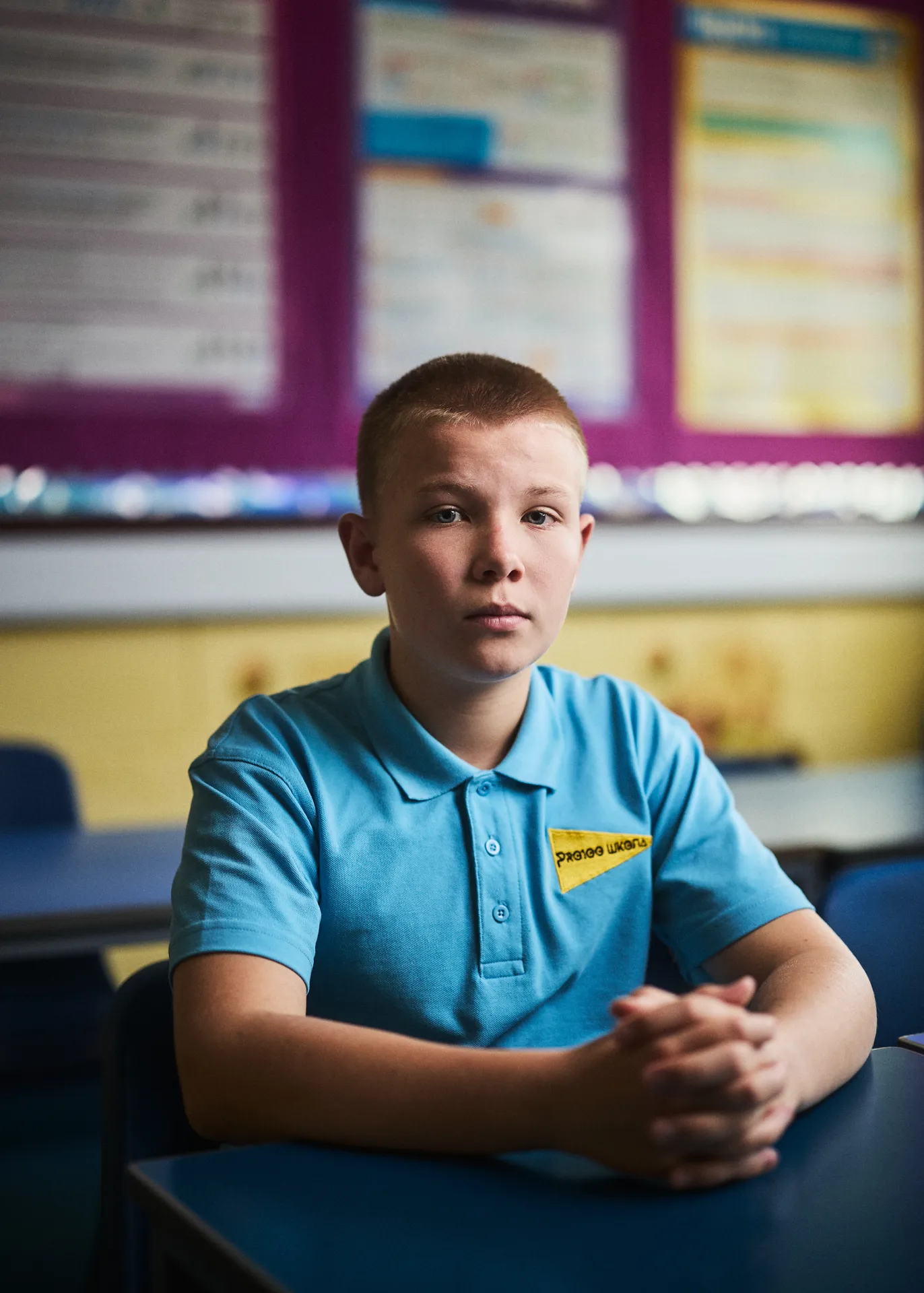 Boy in a blue school polo shirt sitting at a desk in a classroom.