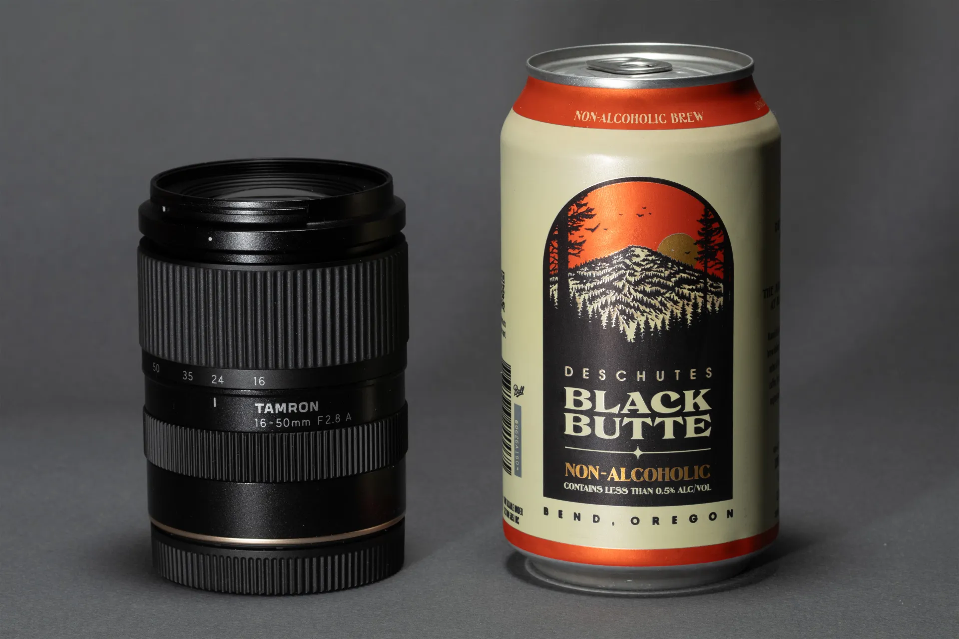 Tamron 16-50mm camera lens beside a Deschutes Black Butte non-alcoholic beer can.
